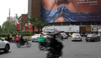 Warga Teheran melintas di depan billboard anti-Amerika Serikat bergambar Donald Trump dan Selat Hormuz di Iran.