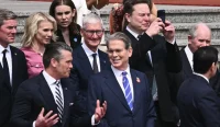 Elon Musk menggunakan ponselnya saat upacara penyambutan di Great Hall of the People, Beijing, disaksikan Pete Hegseth dan Tim Cook.