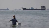 seorang pria memancing di Bandar Abbas dengan kapal-kapal terjebak di Selat Hormuz