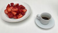 Sepiring stroberi segar dan secangkir kopi hitam di atas meja putih yang dikaitkan dengan penelitian tentang penuaan sel.