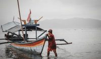 Seorang nelayan menuntun perahu tradisional di pesisir pantai saat biaya operasional melaut meningkat akibat kenaikan harga BBM.