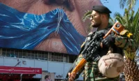Seorang polisi berjaga di depan poster bergambar Donald Trump dengan ilustrasi Selat Hormuz di Teheran, Iran.
