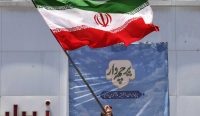 Teks Alt: Warga Iran mengibarkan bendera nasional di Teheran saat perdebatan mengenai kesepakatan damai Iran dan Amerika Serikat semakin memanas