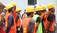 Pekerja mengenakan helm dan rompi keselamatan di area kerja