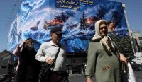 Warga Teheran berjalan melintasi papan reklame propaganda Selat Hormuz di Iran pasca Donald Trump menolak proposal pembukaan jalur pelayaran. Foto: Majid Asgaripour/Reuters. Keyword: Selat Hormuz.