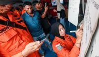 Petugas Basarnas berseragam oranye sedang sibuk mendata dan menulis nama-nama korban tragedi KM Virgo Transport 8 di papan tulis Posko Tanggap Darurat, disaksikan oleh warga yang cemas menanti kabar. Keyword: KM Virgo Transport 8, Basarnas Banjarmasin, Kecelakaan Kapal, Evakuasi Laut Jawa. Kredit Foto: Infuz/AFP.