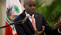 Potret mendiang Presiden Haiti Jovenel Moïse yang mengenakan jas gelap dan dasi merah sedang berbicara dan memberikan isyarat tangan di depan mikrofon pada Maret 2020. Foto arsip ini diambil setahun sebelum kasus pembunuhan Presiden Haiti yang berdarah itu terjadi. Foto: Andrés Martínez Casares/Reuters.