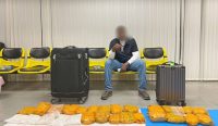 Seorang tersangka duduk di antara koper bawaannya dengan barang bukti puluhan paket kuning berisi 21,3 kg heroin yang disita otoritas Thailand. Tangkapan ini merupakan bagian dari Operasi Lionfish-Mayag IV Interpol yang sukses menyita 650 ton narkoba global, termasuk temuan narkoba etomidate di Indonesia. (Kredit Foto: INTERPOL)