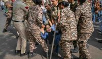 Sejumlah personel kepolisian wanita dan pasukan paramiliter India berseragam kamuflase tampak menahan dan menarik paksa lengan seorang pengunjuk rasa wanita yang berteriak saat terjatuh di jalan aspal, di tengah memanasnya aksi Protes Partai Kecoak di New Delhi. (Kredit Foto: Ritesh Shukla/Getty Images)