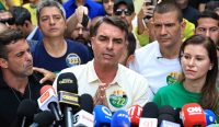 Calon presiden sayap kanan Flávio Bolsonaro memberikan keterangan pers di hadapan puluhan mikrofon wartawan pada hari pemungutan suara Pilpres Brasil di Rio de Janeiro. Ia sukses memberikan kejutan dengan mengungguli petahana Lula da Silva di putaran pertama. Kredit Foto: Buda Mendes/Getty Images.