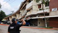 Seorang petugas berseragam hitam meninjau dan memotret kerusakan parah sebuah gedung bertingkat yang ambruk akibat Gempa Panama bermagnitudo 7,7. Tampak lantai bangunan runtuh menimpa mobil di balik garis batas pengaman oranye. (Kredit Foto: Beinvenido Velasco/EPA)