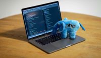 Boneka gajah maskot PHP berdiri di atas keyboard laptop yang menampilkan barisan kode pemrograman, mengilustrasikan ancaman Bug PHP fatal yang membuat jutaan website di seluruh dunia rentan diretas hacker. (Kredit Foto: Ben Griffiths/Unsplash)