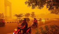 Pengendara sepeda motor menyalakan lampu menembus langit oranye dan pekatnya kabut asap akibat bencana Karhutla di Palangkaraya, Kalimantan. Kredit: Gendes/EPA.