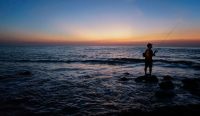 Siluet nelayan memancing di atas karang di tengah ancaman gelombang laut Bali bagian utara yang diprediksi BMKG mencapai 1,4 meter. Foto: Icheer/Unsplash.