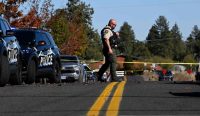 Seorang petugas kepolisian berjaga di balik garis polisi berwarna kuning di depan SD Silver Rail pasca-tragedi mematikan Penembakan Sekolah Oregon. Kredit foto: Joe Kline/AP.