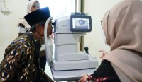 Seorang pria lansia berpeci sedang menjalani pemeriksaan mata dengan mesin medis oleh tenaga kesehatan dalam program operasi katarak gratis untuk menekan angka Kebutaan di Indonesia. Foto: Kementerian Kesehatan RI.