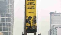 Dua aktivis lingkungan bergelantungan dengan tali membentangkan spanduk kuning raksasa Protes Greenpeace Bundaran HI bertuliskan 'Bencana Makin Parah, Hidup Makin Susah, Apa Kerja Pemerintah?' di Tugu Selamat Datang Jakarta. Foto: Greenpeace.