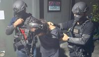 Dua personel pasukan elit Densus 88 Antiteror bersenjata laras panjang mengawal ketat seorang tersangka teroris dengan mata tertutup. Penangkapan ini bagian dari operasi sapu bersih 12 tersangka terorisme jaringan Daulah Islamiyah di enam provinsi. Kredit Foto: Dok. Polri/Istimewa.